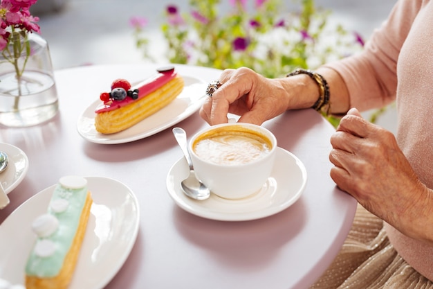 Perto de uma xícara branca cheia de café e éclairs colocados na mesa