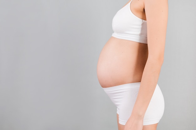 Perto do abdômen da mulher grávida em fundo azul. Menina está vestindo cueca branca. Conceito de maternidade. Copie o espaço