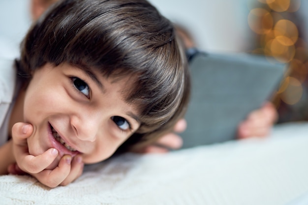 Perto do adorável garotinho latino sorrindo para a câmera enquanto passa um tempo com seu irmão, deitado na cama em casa decorada para o natal. crianças, conceito de férias de inverno