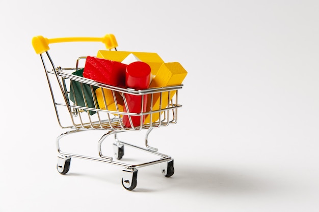 Perto do carrinho de empurrar de supermercado para fazer compras com alça amarela cheia de formas geométricas multicoloridas, isoladas no fundo branco. Conceito de compras. Copie o espaço para anúncio.