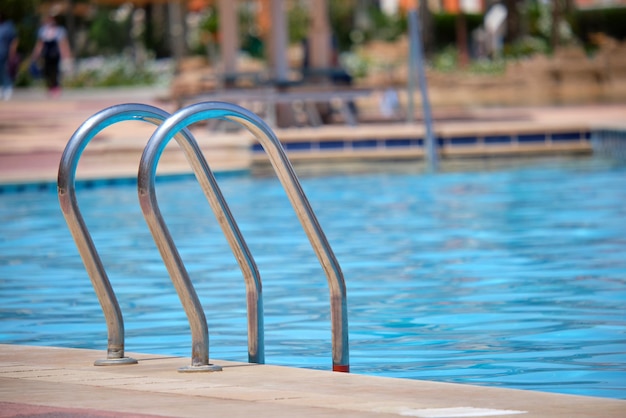 Perto do corrimão de aço inoxidável da piscina descendo para a água clara da piscina da tartaruga. Acessibilidade do conceito de atividades recreativas.