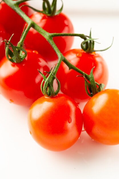 Perto dos saborosos tomates vermelhos maduros no galho verde, deitado na superfície branca e com gotas de água sobre eles
