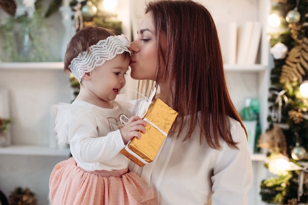 Perto feliz jovem mãe e linda filha, dando um presente de Natal e abraçando. Conceito de férias de natal