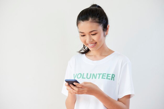 Pertty sonriente joven enviando mensajes de texto a otros voluntarios de su organización