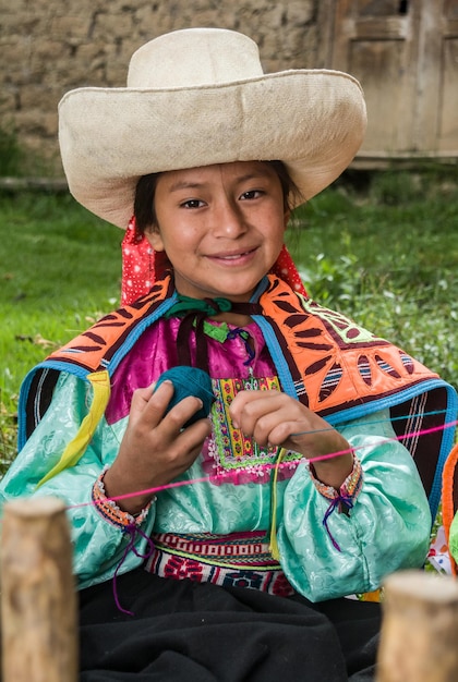 Peruanische Andenmädchen, die Webereien machen und in ihrer Stadt und ihren Häusern mit farbiger Kleidung posieren