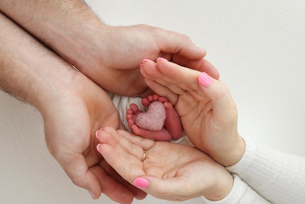 Pés calcanhares de um recém-nascido Pé infantil nas mãos da mãe pai pais com um coração rosa de malha As pernas da criança nos braços da mãe e do pai Em um fundo branco