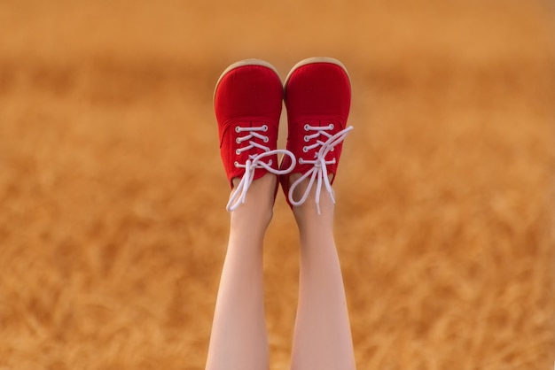 Pés com sapatos vermelhos para cima. Pernas finas femininas no campo de trigo.