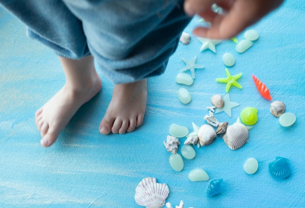 Pés de bebê em fundo de verão de conchas do mar Muitas estrelas do mar de conchas diferentes em um fundo de traços de tinta azul Lugar para texto