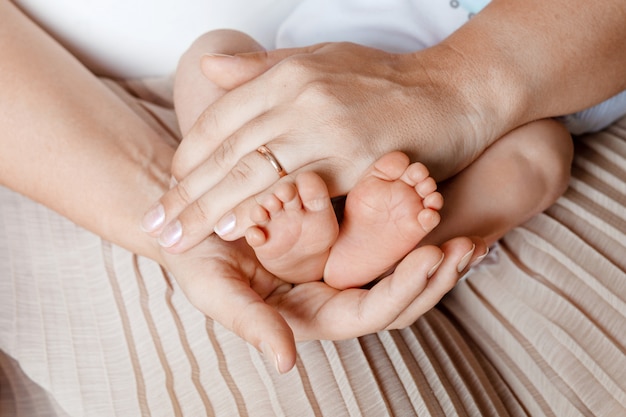 Pés de bebê nas mãos da mãe. os pés do bebê recém-nascido minúsculo na fêmea deram forma ao close up das mãos. mãe e filha. conceito de família feliz. bela imagem conceitual de maternidade