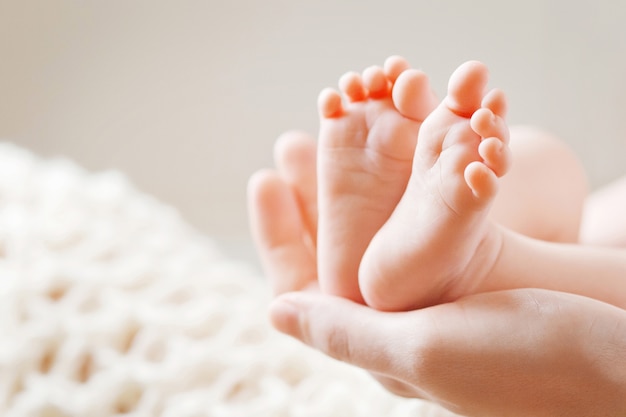 Pés de bebê nas mãos da mãe. Os pés do bebê recém-nascido minúsculo no close up dado forma fêmea das mãos. Mãe e filha.