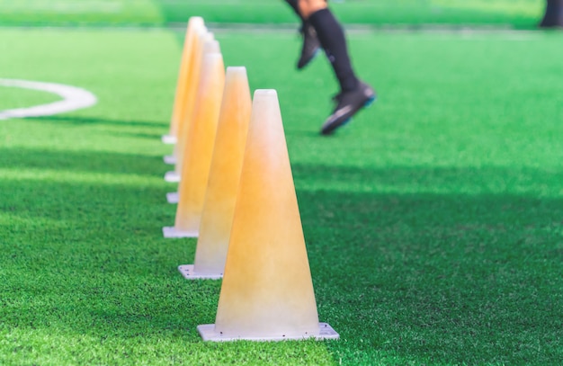 Pés de crianças com botas de futebol treinando no cone de treino no chão de futebol