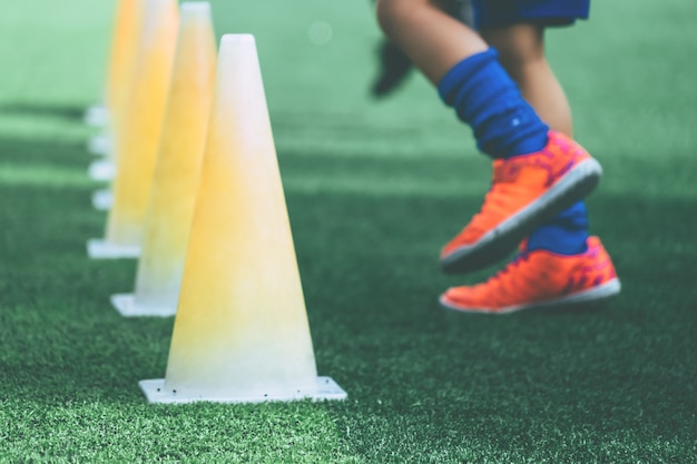 Pés de crianças com botas de futebol treinando no cone de treino no chão de futebol