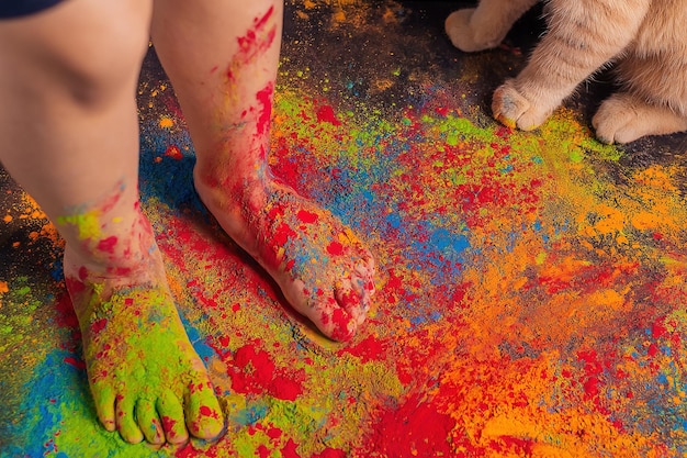 pés de crianças espalhados com cores Holi brilhantes multicoloridas e patas de gato nas proximidades, copie o espaço.