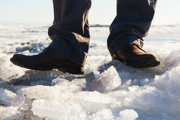 Pés de homem com botas marrons e calças cinza no mar congelado