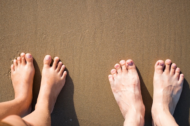 Pés de homem e mulher na praia marrom arenosa.