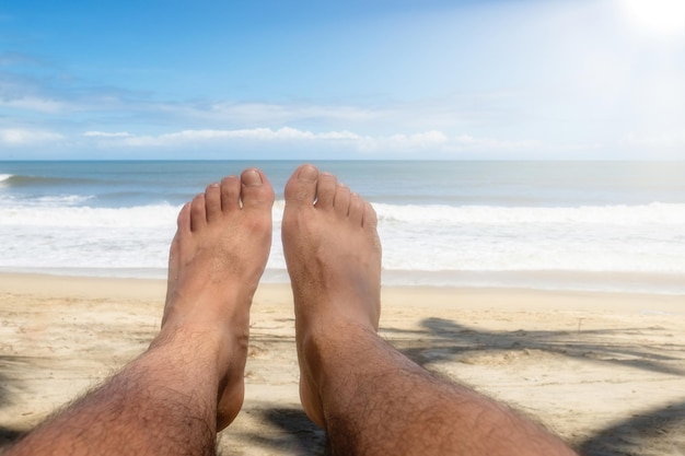 Pés de homem na praia com o mar e o céu azul ao fundo com copyspace