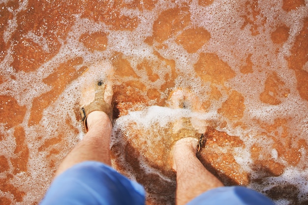 Pés de homens em sandálias na praia homem de shorts jeans se levanta e olha para seus pés na areia que era ...