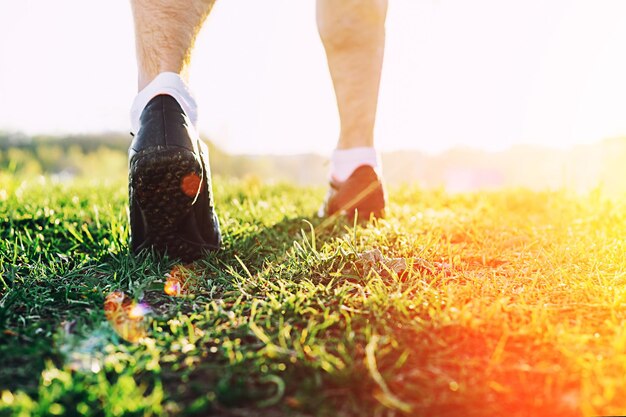 Pés de jovem atleta correndo no parque closeup no sapato Treino de corredor de atleta de fitness masculino no conceito de bem-estar ao pôr do sol Conceito de estilo de vida saudável esportivo