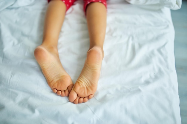 Pés de menina cobertos com lençol branco dormindo em uma cama confortável