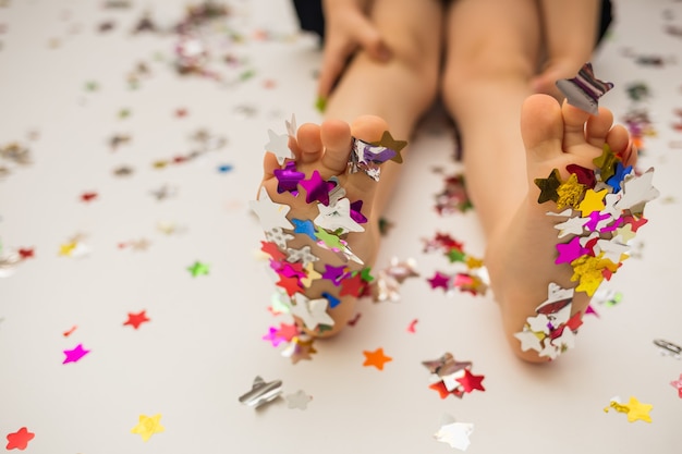 Pés de menina em estrelas coloridas de confete em um fundo branco