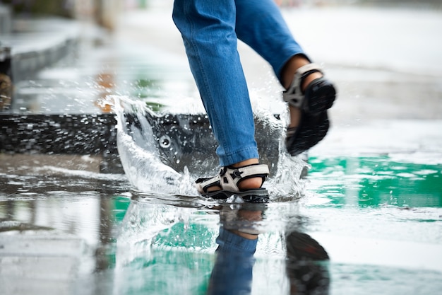 Pés de mulher correndo em poças com respingos de água em um dia chuvoso