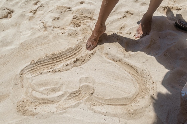 Pés de mulher desenhando um coração na areia. mulher apaixonada desenhando um coração na praia.