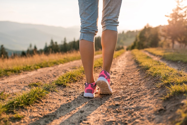 Pés de mulher feminina atleta corredor correndo na estrada de montanha sob a luz do sol