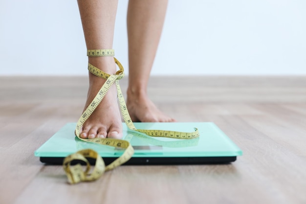 Foto pés de mulheres pisando em balanças amarradas com fita de medição