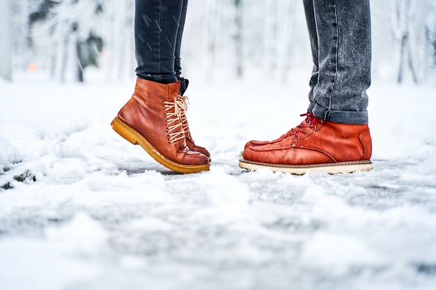 Pés de um casal na calçada com neve em botas marrons