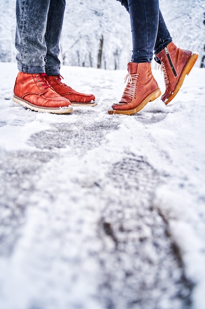 Pés de um casal na calçada com neve em botas marrons