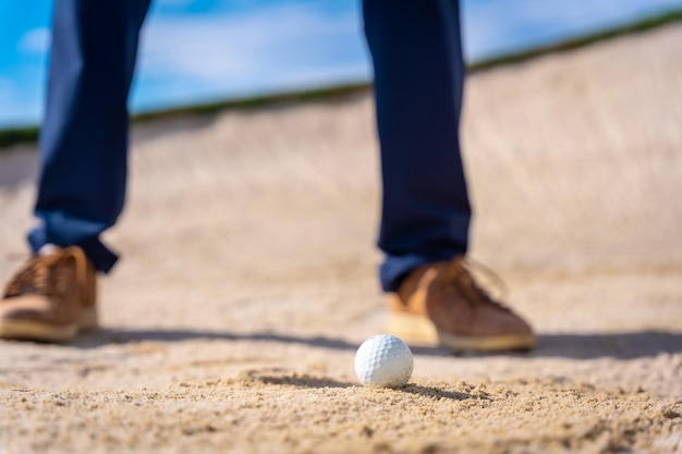 Pés de um homem jogando golfe no bunker batendo na bola com o bastão de cunha