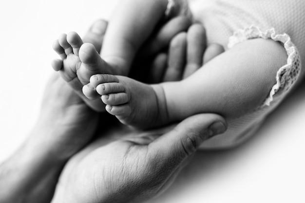 Pés de um recém-nascido nas mãos de um pai, pai. Fotografia de estúdio, preto e branco. Conceito de família feliz. Foto de alta qualidade