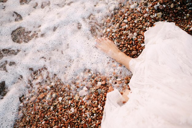 Pés descalços da noiva em uma praia de seixos lavada pela água do mar