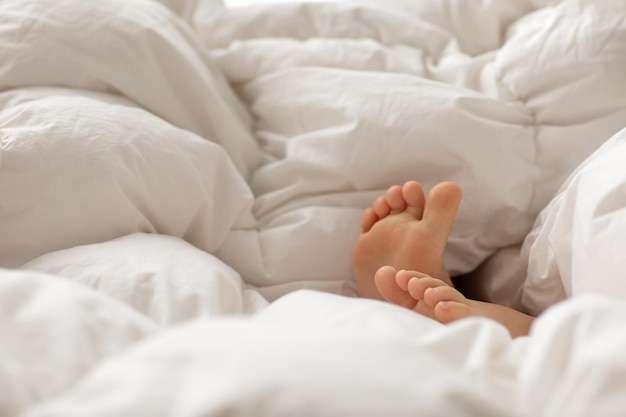 Pés descalços de criança fria e quente de inverno em cobertor branco grande e fofo na cama