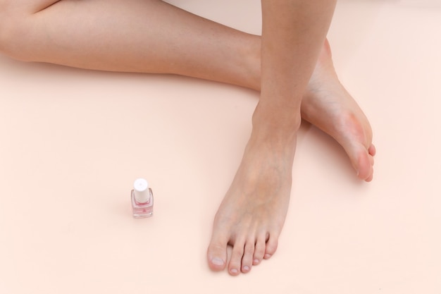 Pés descalços femininos, frasco de esmalte em um fundo bege. conceito de cuidados de beleza