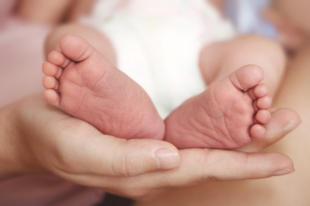 Pés do bebê recém-nascido na palma da mão da mãe