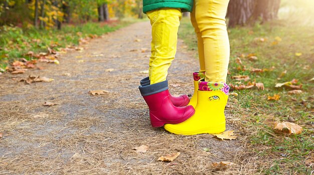 Pés em botas de borracha vermelhas e amarelas de mãe e filha na floresta de outono. sazonalidade, estações, folhas secas de bordo caídas, caminhada em família, sentimento de amor e carinho, paternidade