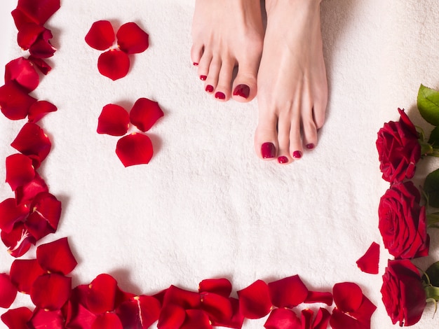 Pés femininos bonitos com uma pedicure vermelha em uma banheira com sal e pétalas de rosa. conceito de cuidados de spa e pele.