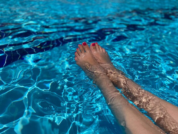 Pés femininos com esmalte vermelho perto da borda da piscina