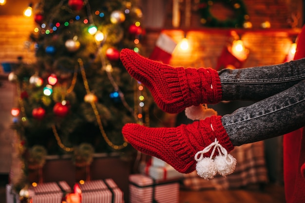 Pés femininos com meias vermelhas alegres, árvore de Natal com decoração