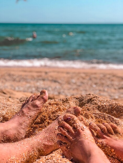 Pés femininos e masculinos em um close-up da praia de areia de concha num contexto de água do mar azul. conceito de férias e viagens.