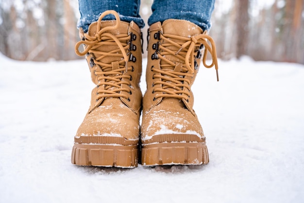 Pés femininos em botas amarelas na neve em uma floresta de neve