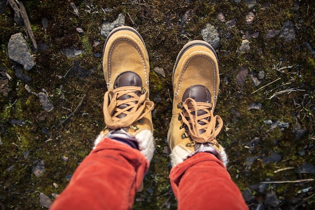 Foto pés femininos em botas de camurça amarela ficam em musgo com pedras. vista do topo. fechar-se