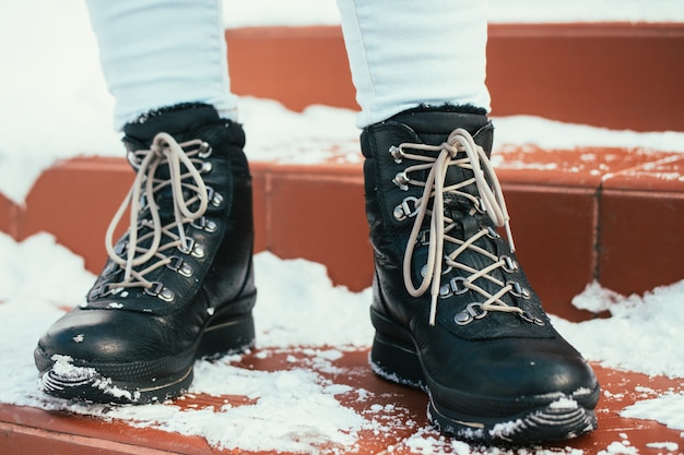 Pés femininos em botas de inverno com atacadores estão nas escadas na neve