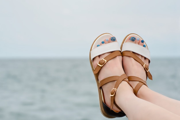 Pés femininos em sandálias com uma manicure no mar