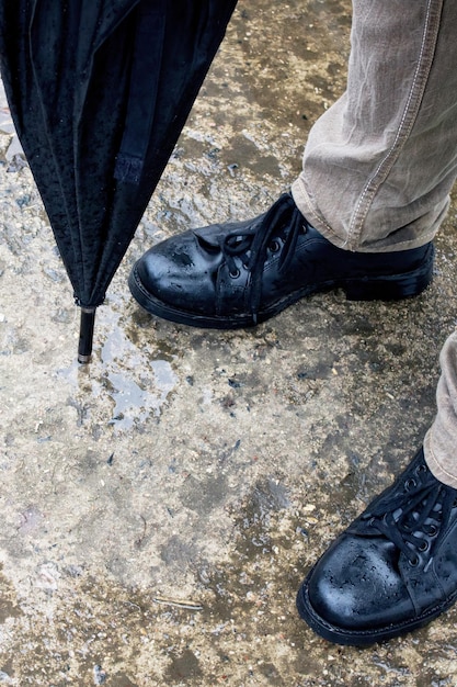 Pés masculinos em botas e guarda-chuva no asfalto