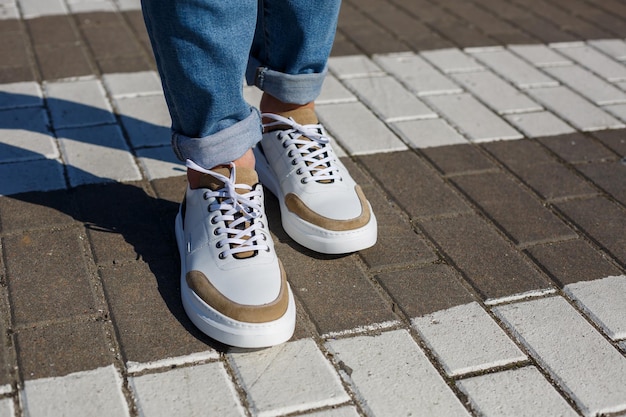 Pés masculinos em tênis branco do dia a dia feitos de couro natural com cordão.