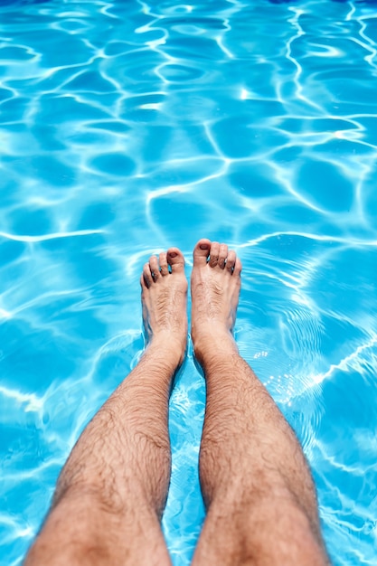 Pés masculinos sobre a água azul em uma piscina sob o sol, close up