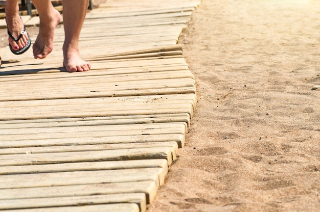 Pés no caminho de madeira para a praia de areia.