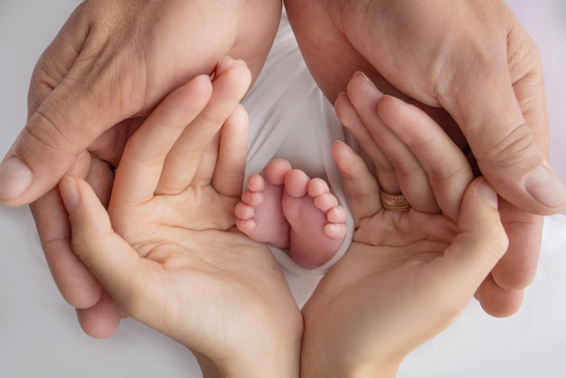 Pés pequenos de um recém-nascido nas mãos dos pais Amando as palmas das mãos da mãe e do pai Imagem conceitual da paternidade Closeup foco seletivo Fotografia profissional um fundo branco